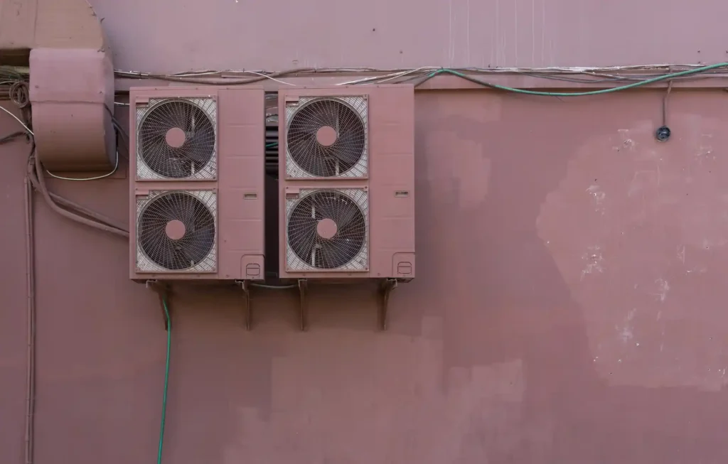 Two outdoor air conditioning units mounted on a painted exterior wall