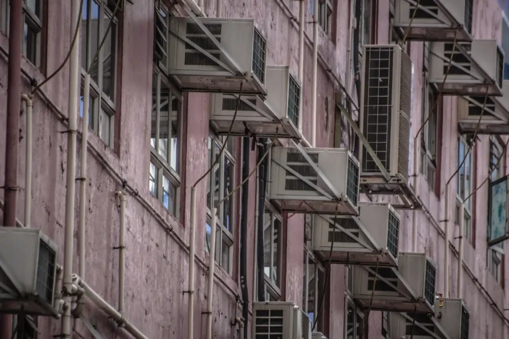 Multiple window air conditioner units installed along a pink building facade