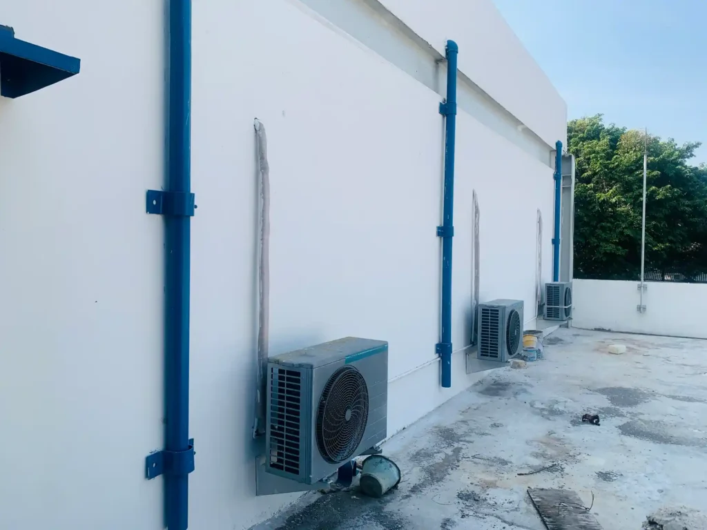 Three outdoor air conditioning units installed along the exterior wall of a building