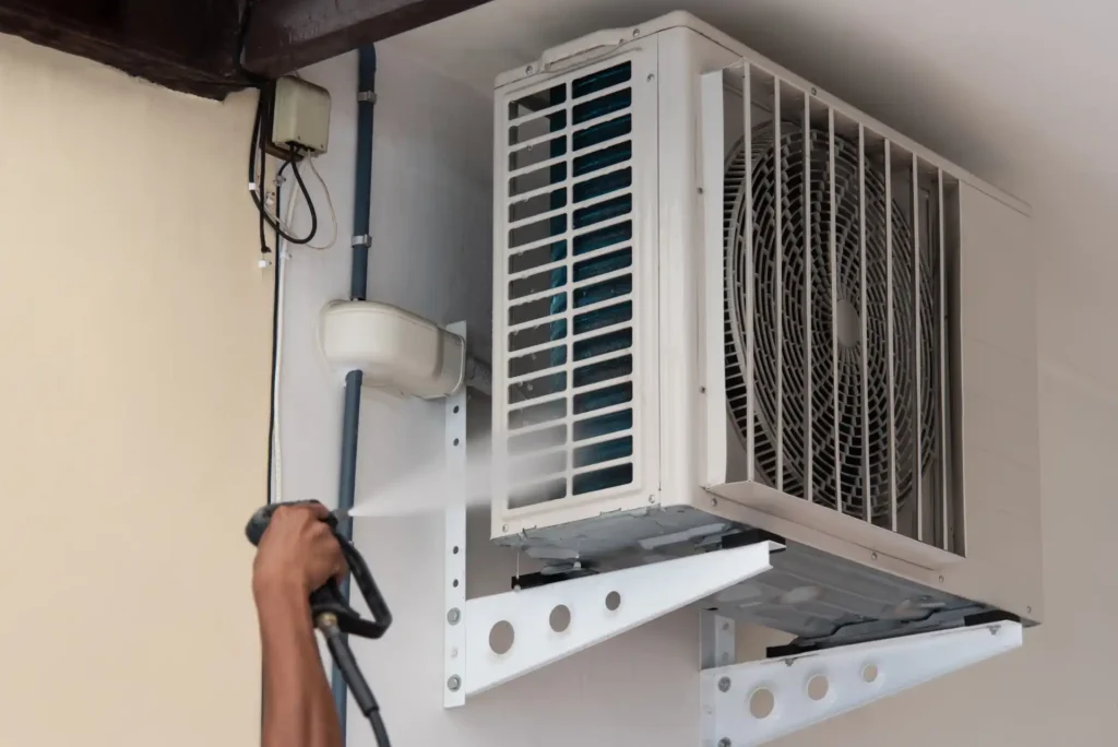 Technician pressure washing an outdoor AC condenser unit